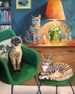 a painting of a siamese cat on a green velvet chair, a ginger tabby on a green velvet stool and a grey tabby sitting on a dresser with a warm lamp. there is a bookcase, a candle and a vase of lavender
